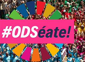 El aro de los Objetivos de Desarrollo Sostenible y hashtag #ODSéate, con gente de fondo.